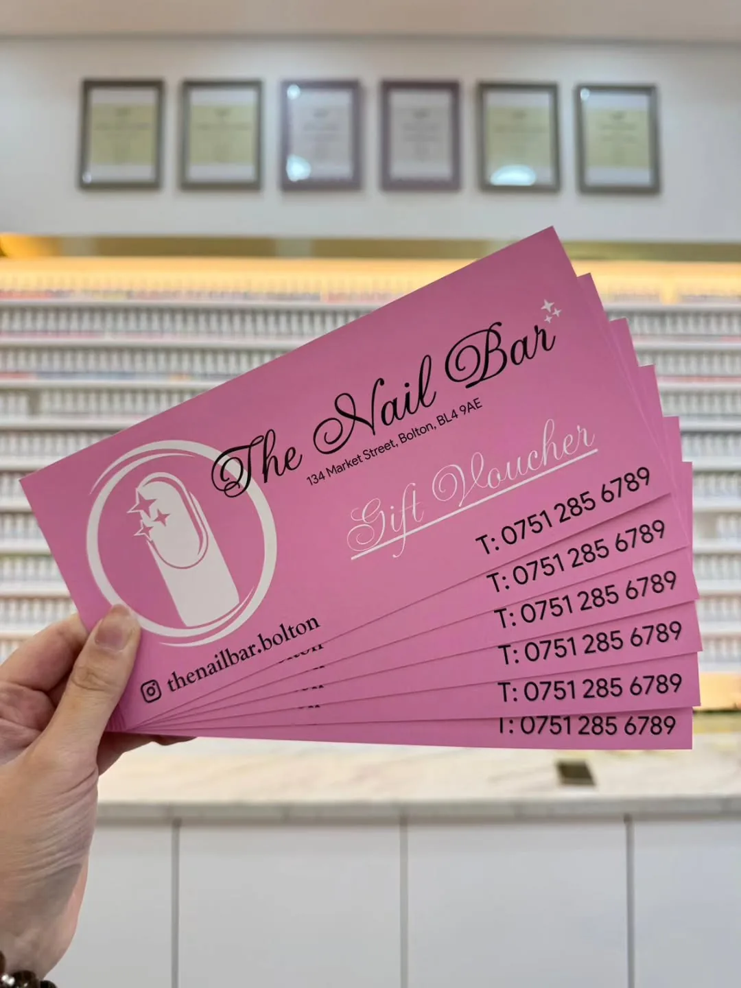 A fan of pink The Nail Bar gift vouchers held up in front of the salon's polish wall