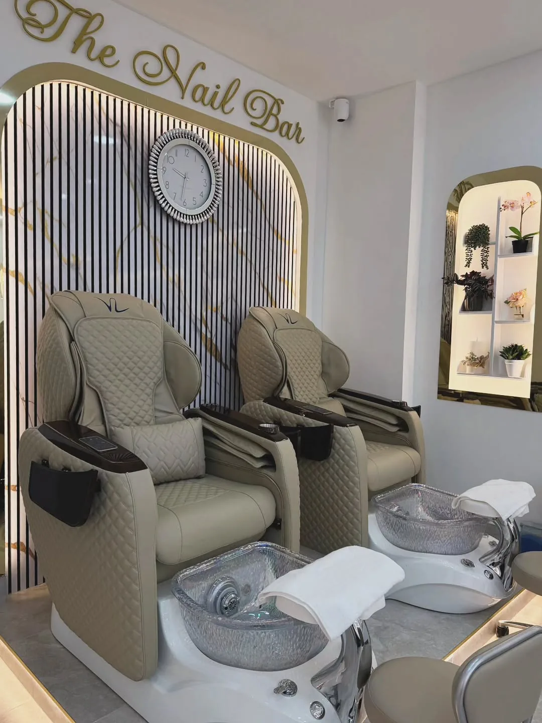 The pedicure suite at The Nail Bar, with two cream leather massage chairs beneath the gold script signage